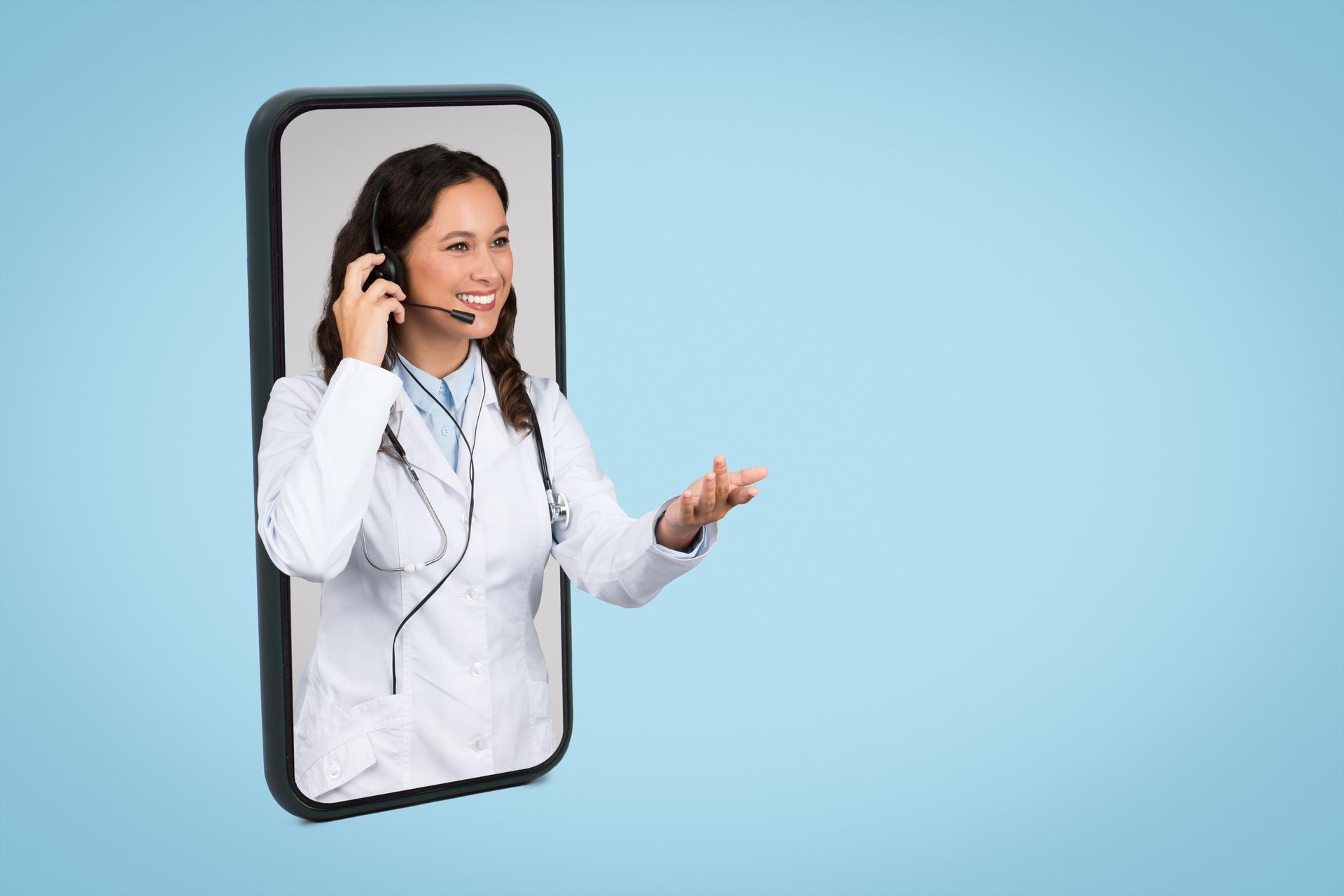 Friendly caucasian woman doctor wearing headset peeking out of huge smartphone screen over blue background, free space